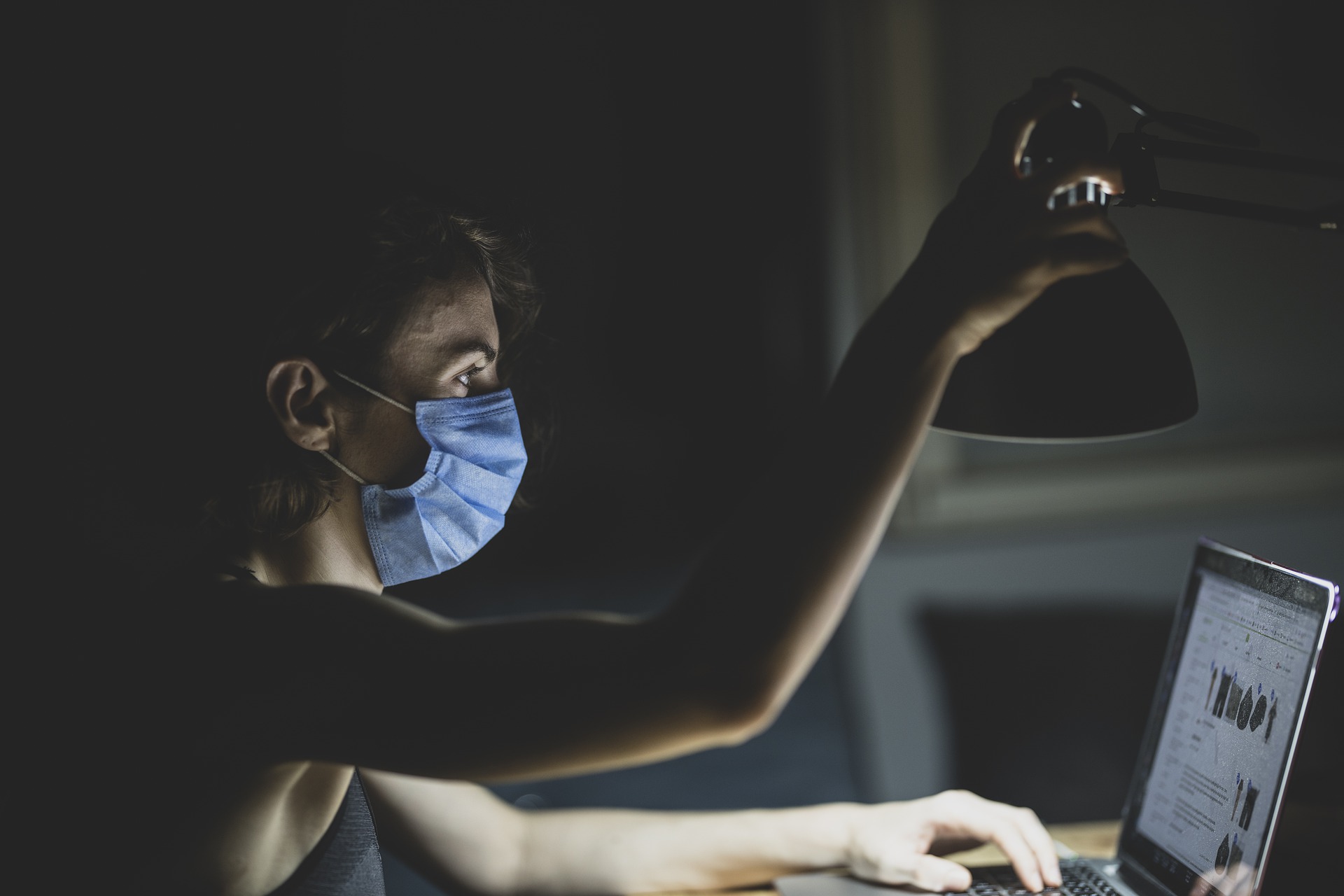 Joven con mascarilla prendiendo lámpara en escritorio